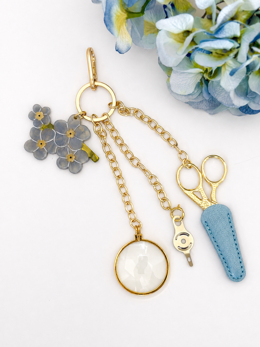 Blue Blooms Tool Chain: blue flower cluster charm, gold embroidery scissors in a powder-blue leather sheath, needle threader, and 5x magnifier on a gold clasp