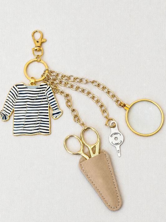 Breton Stripe Tool Chain: Sara Fitz striped shirt enamel charm, gold stork scissors in a taupe leather sheath, needle threader, and 5x magnifier on a gold clasp