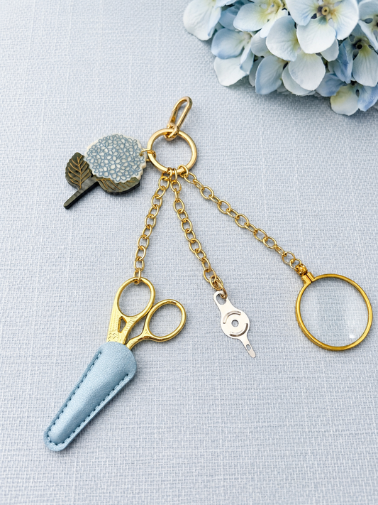 Gold stork scissors, folding magnifier and threader on a gold chain with a hydrangea bloom charm
