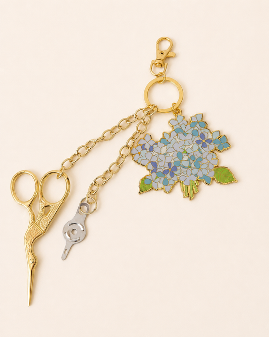 Sara Fitz hydrangea bloom enamel charm on a gold chain with gold stork embroidery scissors and a needle threader