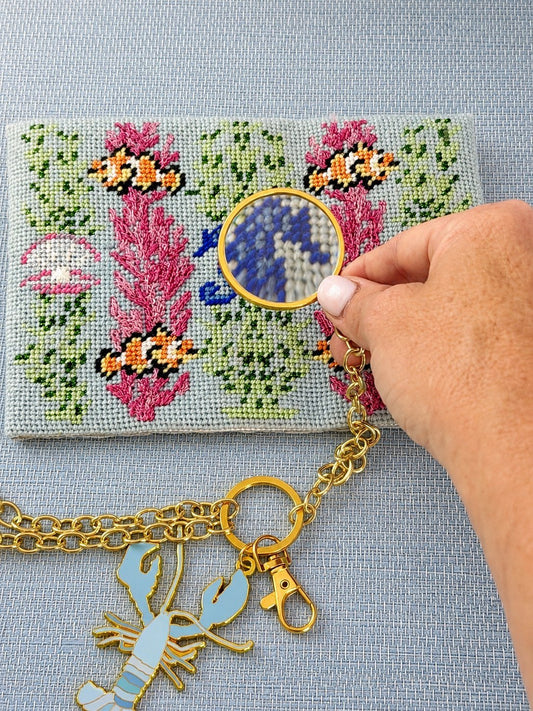 The 5x magnifier held over a stitched needlepoint canvas, lobster chain in the foreground