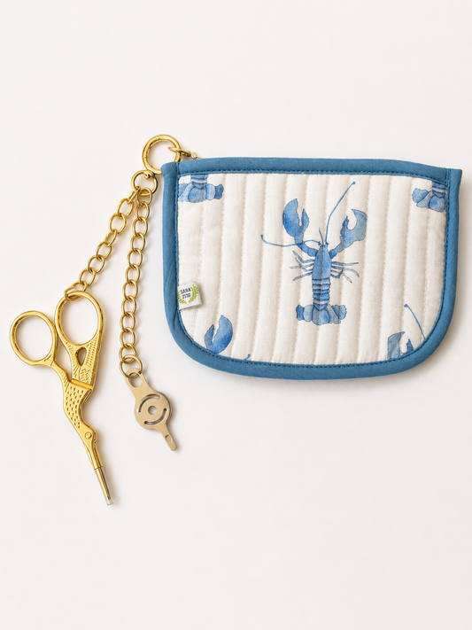 Sara Fitz quilted lobster pouch with gold chain, gold stork embroidery scissors and a needle threader