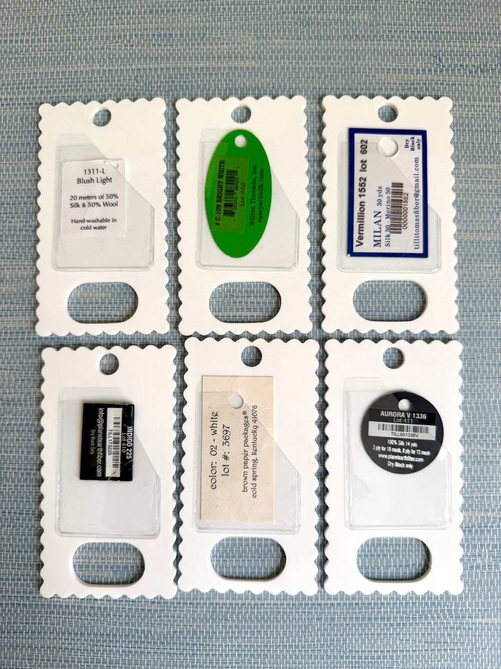 The backs of six thread drops, each pocket holding a different thread tag
